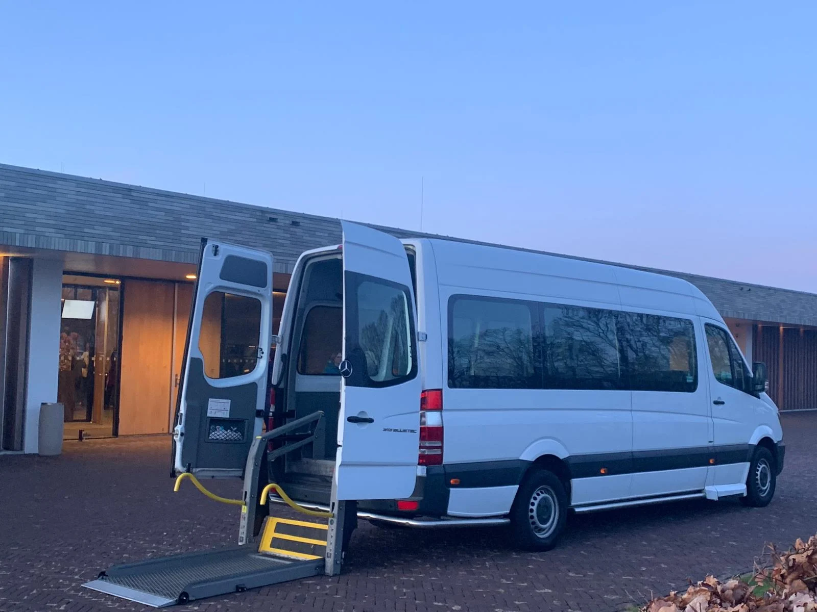 Onze aangepaste taxibus met geopende deuren en rolstoellift